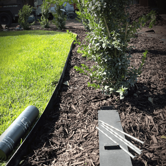 metal edging installed to separate mulch and grass. extra piece of edging is laying in mulch with stakes. green shrub plants