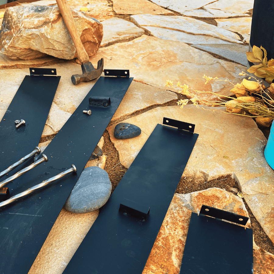 black metal edging laying on flagstones with stainless steel anchoring spikes and a hammer